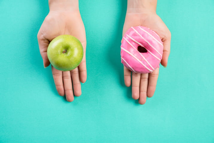 One hand holding an apple and one hand holding a donut