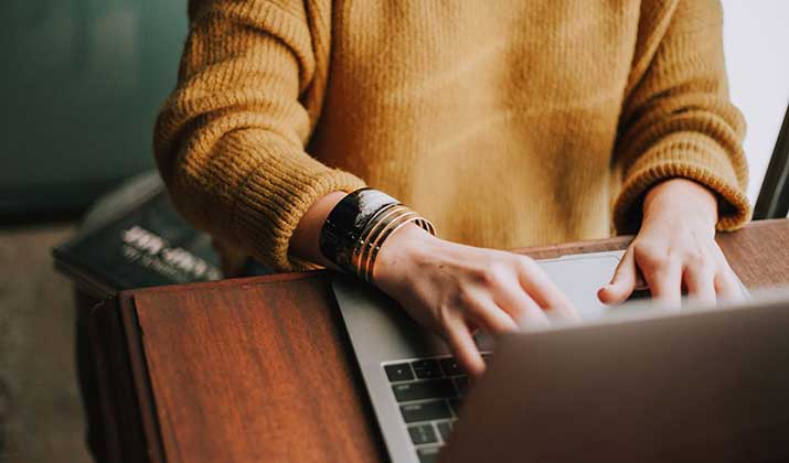 female typing on laptop with orange sweater