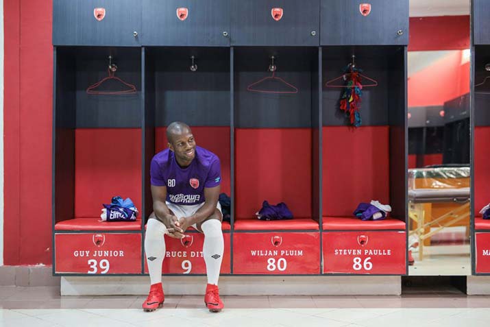 Griffith student and elite athlete Bruce Djité seated in a football club locker room