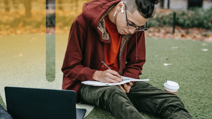 Person sitting on ground writing OUA