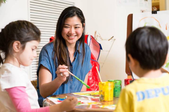 Nikki Bilog, a young teacher, sitting and painting with two children