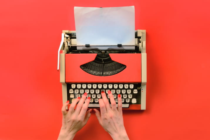 Hands typing on a vintage red typewriter against a bright red background