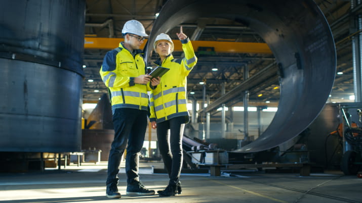 Two engineers in high vis vests inside an industrial space discussing their work