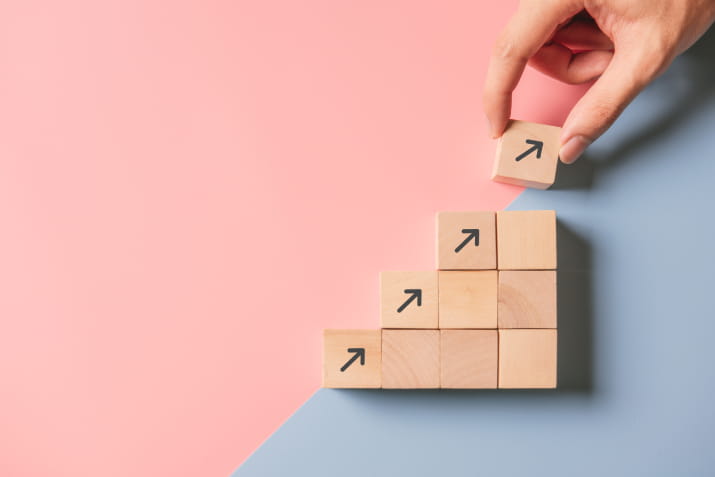 A hand arranging building blocks. Four of the blocks contain arrows pointing up