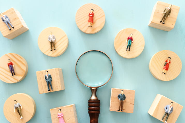 A magnifying glass surrounded by small figurines of people
