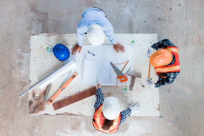 A bird's eye view of an architect and contractors going over blueprints