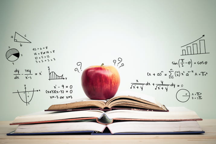 An apple sitting on an open book surrounded by equations