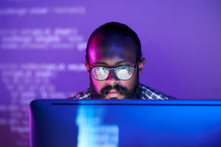 A man looking at code on a computer in a dark room