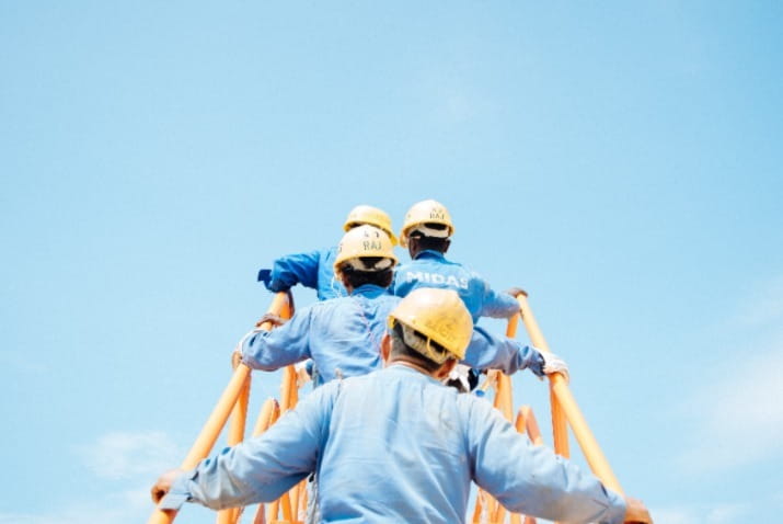 Construction workers with hard hats climbing scaffolding