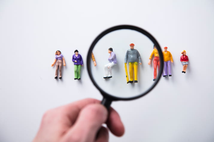 A hand holding a magnifying glass over people figurines