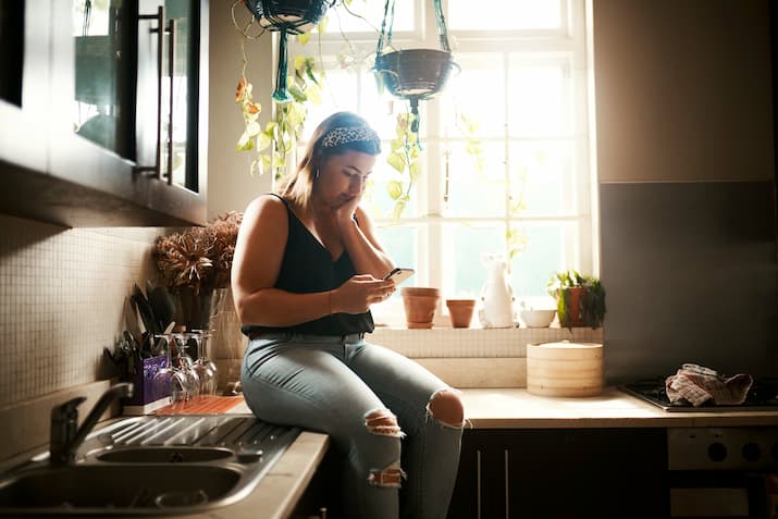 Young woman reading text message on kitchen bench