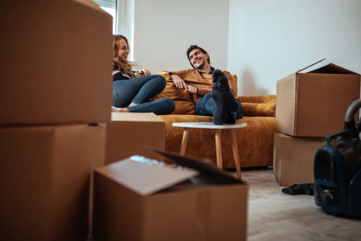 A woman and man taking a break in a living room surrounded by moving boxes