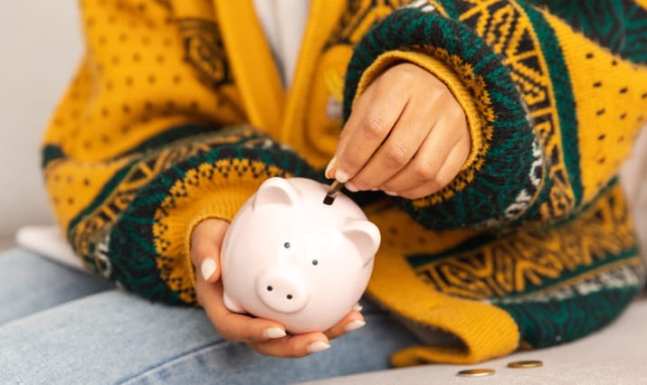 A faceless person in a yellow sweater putting a coin into a piggybank