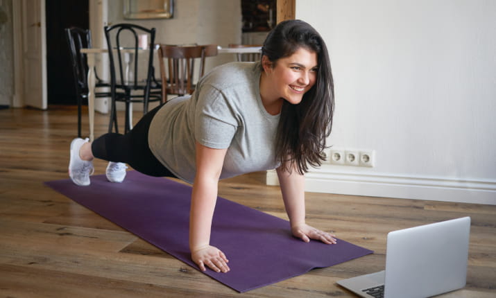 A smiling woman doing yoga in front of a laptop