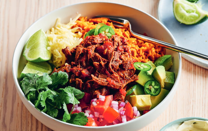 Slow cooked Mexican beef garnished with rice, coriander, jalapenos, lime, avocado and salsa