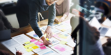 A team of professionals collaborating on papers spread over a table with colourful sticky notes.
