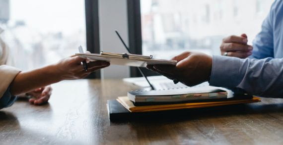 Two people exchanging documents over a table