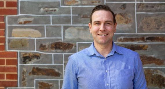 Open Universities Australia student David wearing professional clothes standing in front of a brick wall.