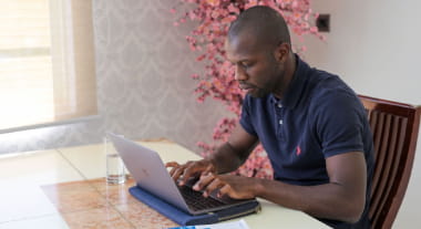Open Universities Australia student, Bruce, sitting at a table, using a notebook computer and a textbook.